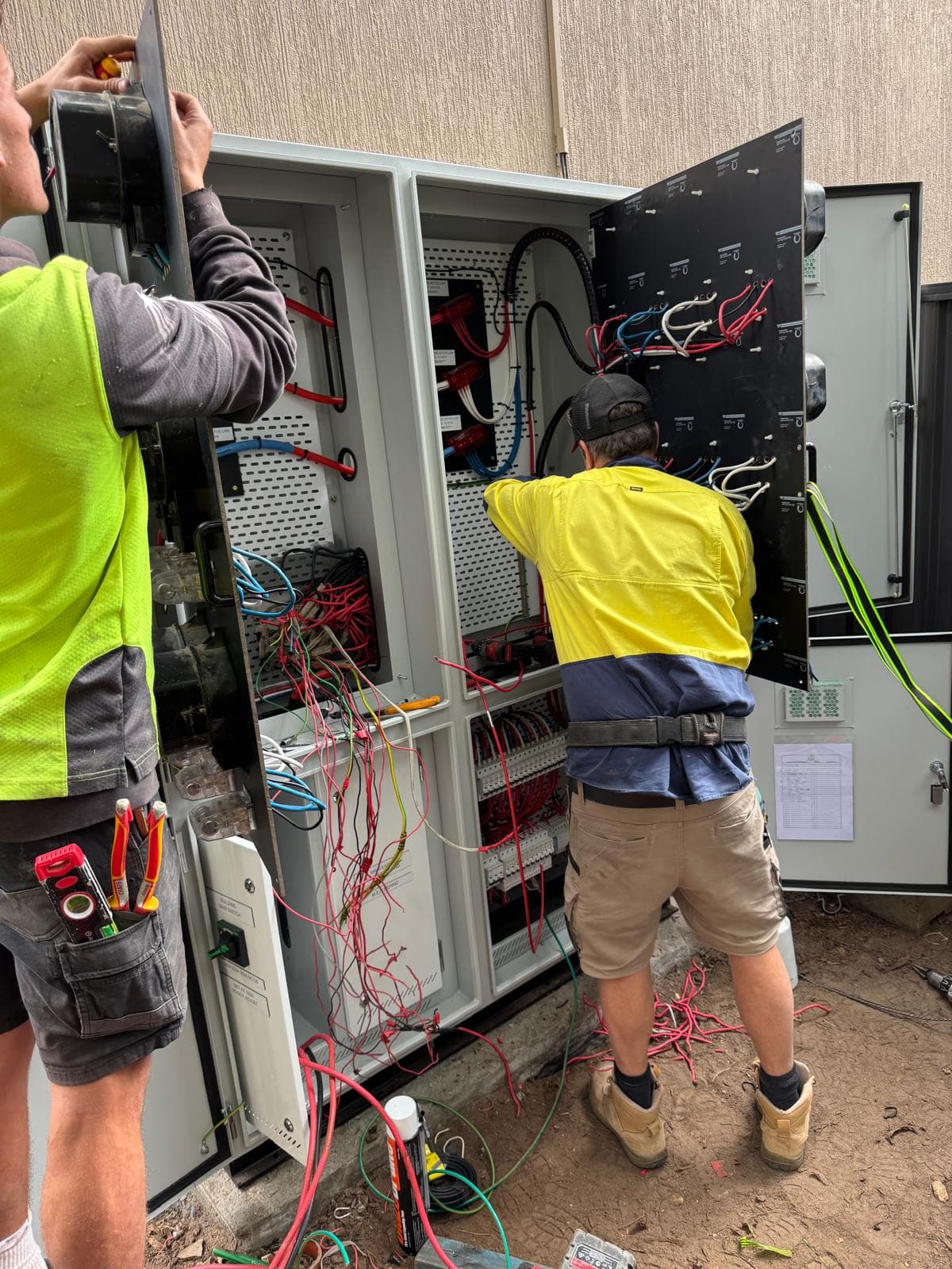 Two electricians working inside the open switchboard mid-changeover